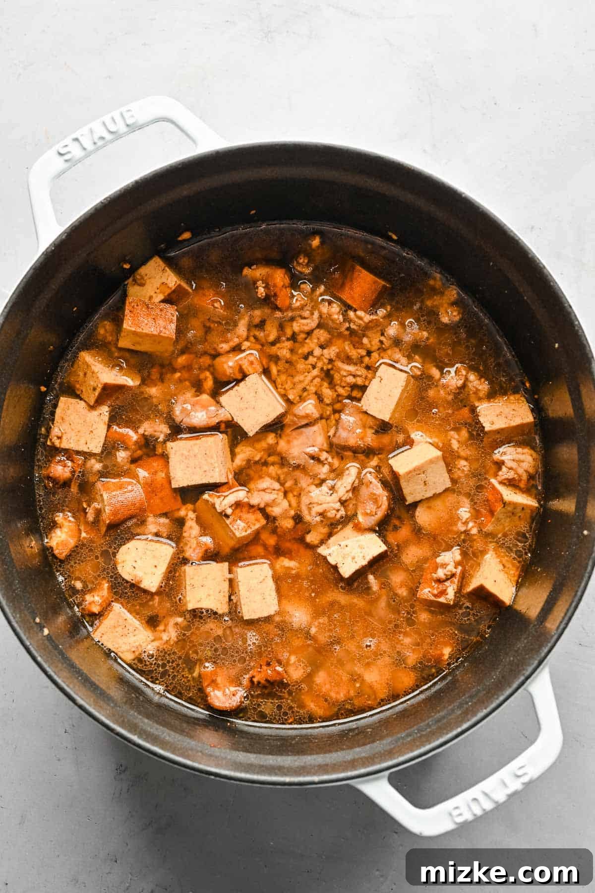 Adding water to the Taiwanese braised minced pork mixture for simmering. Water being poured into a pot containing the braised minced pork, mushrooms, and tofu, preparing for the simmering phase.