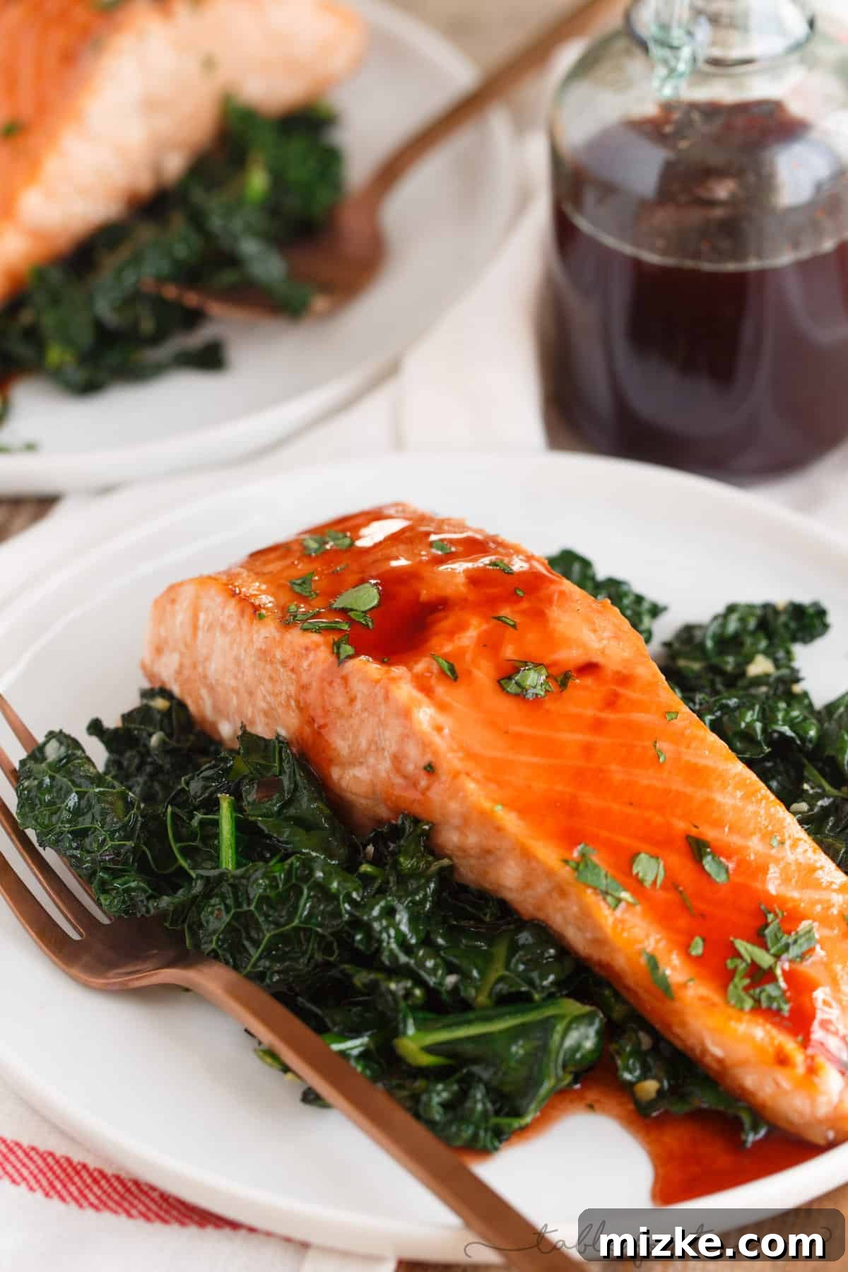Close-up of perfectly cooked salmon with a shiny cherry chipotle glaze, garnished with fresh herbs, ready to be served.