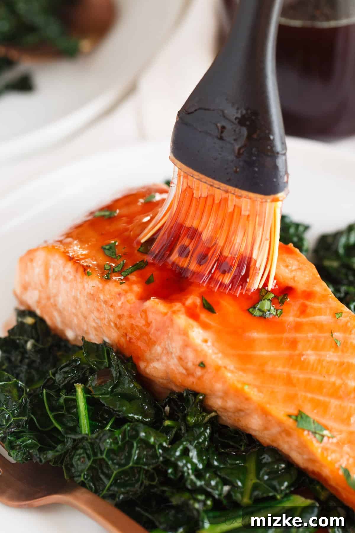 A chef's hand drizzling generous amounts of cherry chipotle glaze over a beautifully pan-seared salmon fillet.