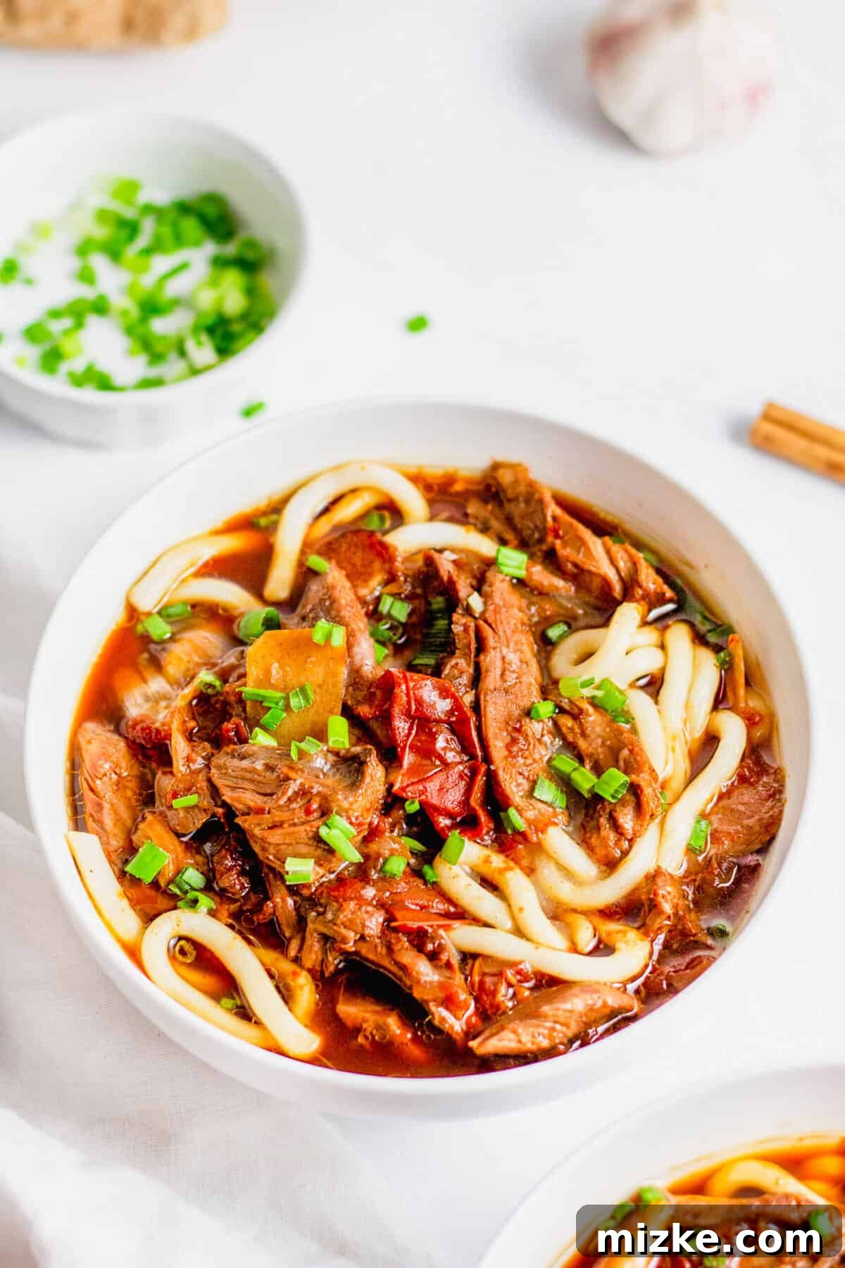 A comforting bowl of Instant Pot Taiwanese Beef Noodle Soup, perfect for any season. Close-up of a bowl of Taiwanese Beef Noodle Soup, artfully topped with finely sliced green onions, ready for serving