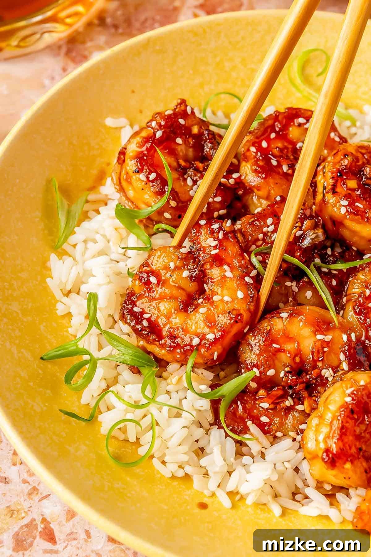 Glazed Honey Garlic Shrimp Stir Fry 4 A pair of wooden chopsticks delicately holding a glistening honey garlic shrimp, poised over a bed of white rice, illustrating the perfect serving suggestion.