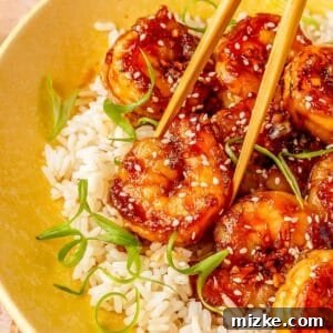 Glazed Honey Garlic Shrimp Stir Fry 5 A close-up of a single honey garlic shrimp held by wooden chopsticks over white rice, perfectly illustrating the finished dish.