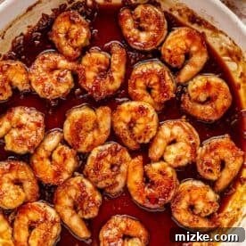 Glazed Honey Garlic Shrimp Stir Fry 10 Cooked shrimp being added back into the thickened honey garlic sauce in a white skillet, showing the final coating step.