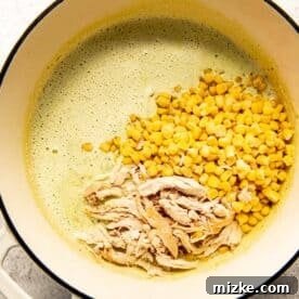 Shredded chicken and frozen corn being added to the creamy soup in the Dutch oven.