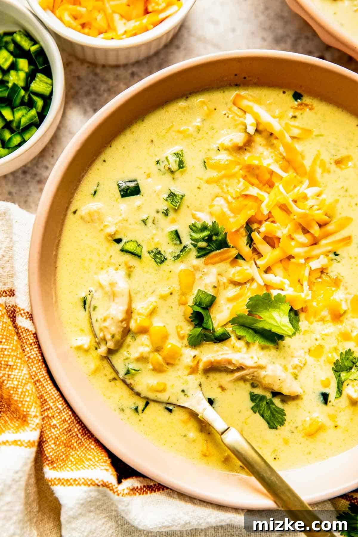 Southwest Chicken Poblano Chowder 4 A close-up of a spoon scooping creamy chicken poblano soup, revealing chunks of shredded chicken and bright frozen corn.