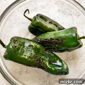 Charred poblano peppers steaming in a clear bowl.