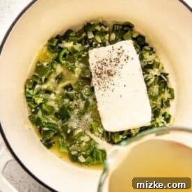 Chicken stock being poured into a Dutch oven with cream cheese, onion, and poblano mixture.