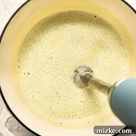 An immersion blender smoothly blending the soup directly in the Dutch oven.
