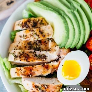 A colorful grilled chicken salad with rosemary, fresh vegetables, and avocado.