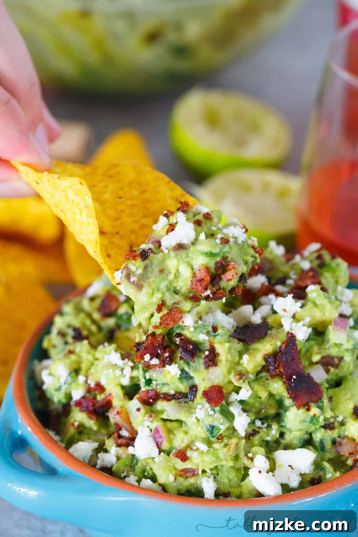 Smoked Poblano and Black Pepper Bacon Guac 2 A vibrant bowl of loaded guacamole featuring charred poblano peppers, crispy bacon bits, and creamy queso fresco, served alongside a refreshing glass of White Zinfandel.