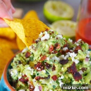 A close-up of Charred Poblano and Peppered Bacon Guacamole in a bowl, showcasing its delicious texture and toppings.