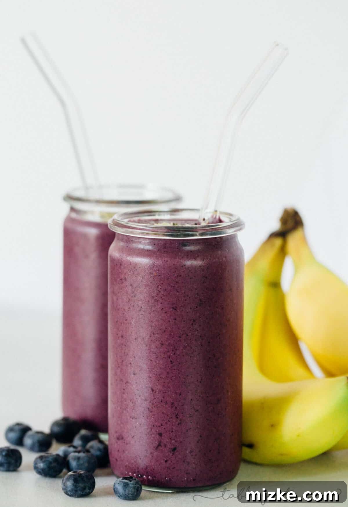 Berry Banana Bliss 4 A vibrant and thick blueberry banana smoothie poured into a glass, ready to be enjoyed. Highlighted with a spoon, showing its creamy consistency.