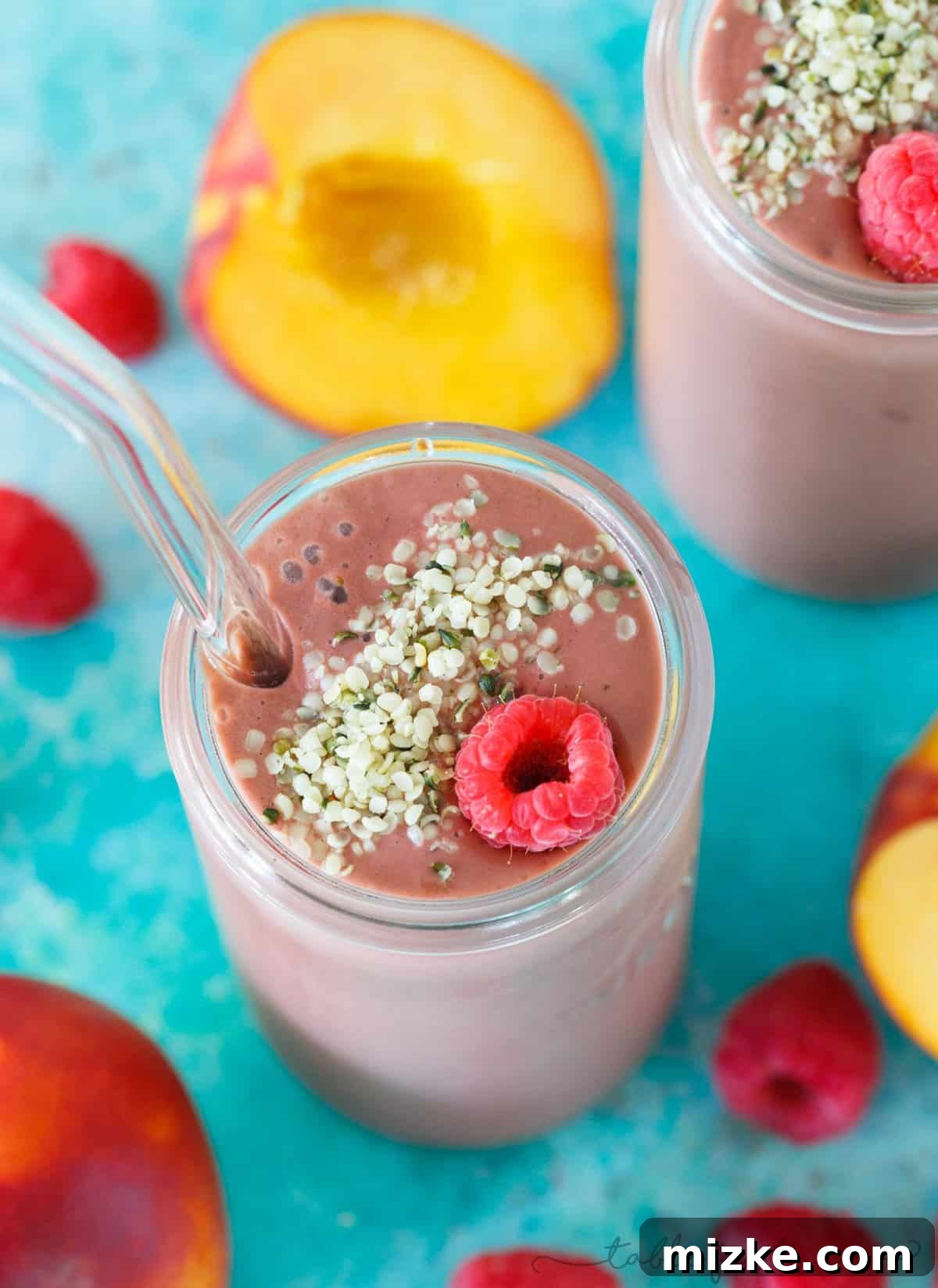 Berry-Peachy Green Power Smoothie 2 A beautifully blended raspberry peach spinach smoothie, showcasing its vibrant pink hue with no visible traces of spinach, topped with fresh raspberries and peach slices.