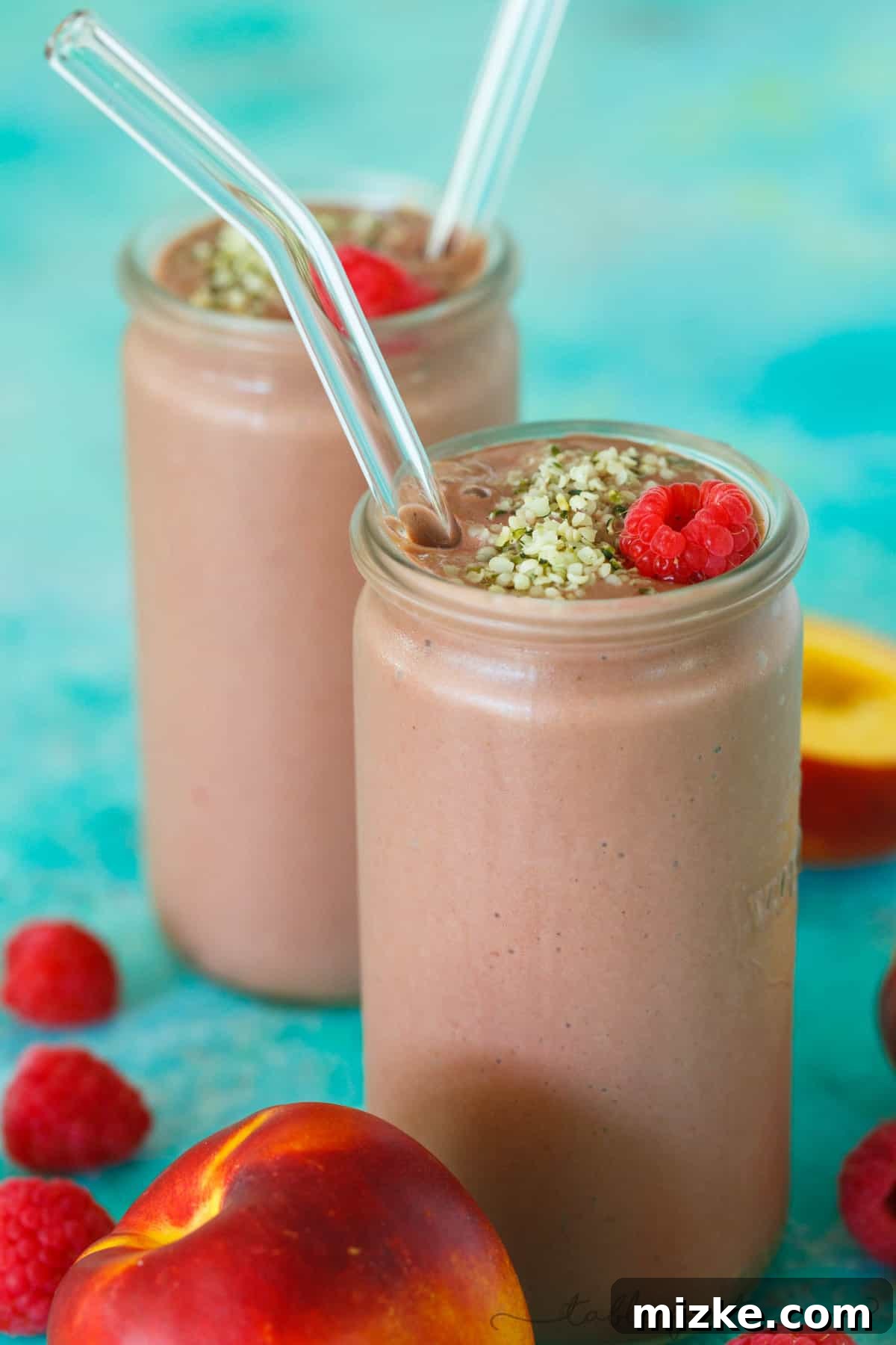 Berry-Peachy Green Power Smoothie 5 Four tall glasses of freshly made Raspberry Peach Spinach Smoothie, with one glass featuring a garnish of raspberries and peaches, signifying a refreshing summer drink.