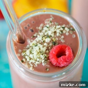 A vibrant pink Raspberry Peach Spinach Smoothie in a glass, with fresh raspberries and peach slices, highlighting its appealing appearance without any visible spinach.