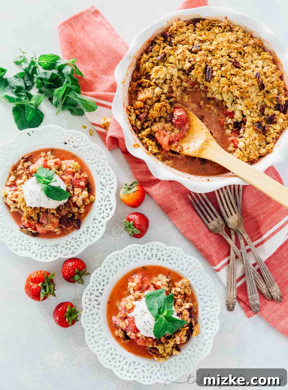 A vibrant Strawberry Mint Crisp, featuring a golden-brown oat topping over juicy red strawberries, ready to be served with a dollop of vanilla ice cream. This easy dessert is perfect for using fresh garden mint and seasonal strawberries.