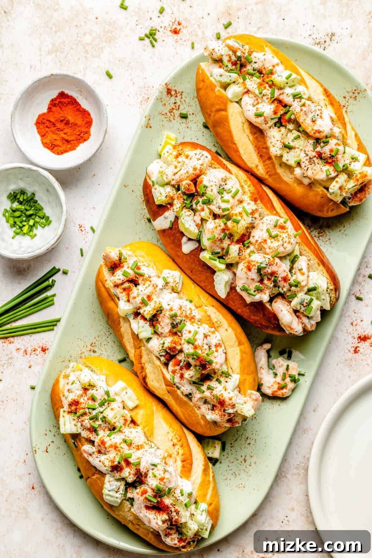 Savory Shrimp Wraps 2 Four perfectly assembled creamy shrimp rolls lined up on a vibrant green plate, generously garnished with fresh green chives, showcasing a delicious summer meal.