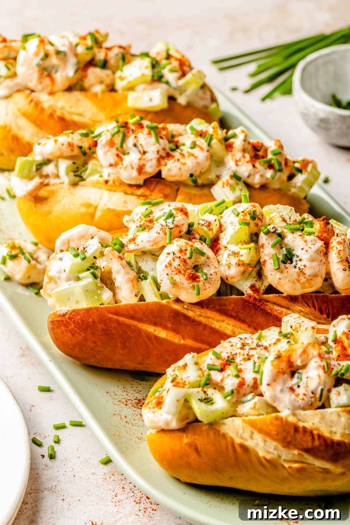 Savory Shrimp Wraps 4 Several beautifully prepared shrimp rolls displayed in a graceful diagonal line on a vibrant green serving plate, showcasing their golden toasted brioche buns and generous, fresh filling.