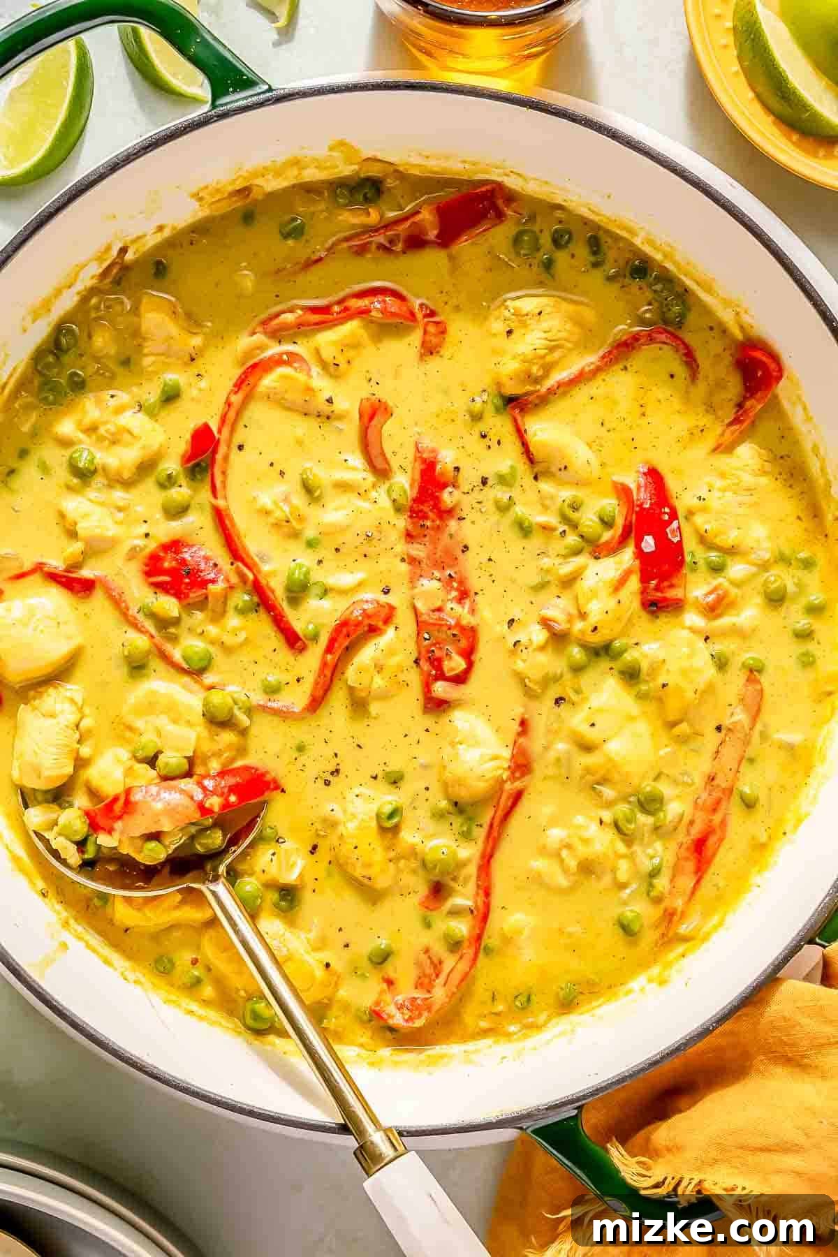Spicy Thai Green Curry Chicken Rice Bowl 3 A creamy green curry in a pot with chicken, red bell peppers and green peas, accompanied by a serving spoon.