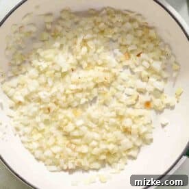 Spicy Thai Green Curry Chicken Rice Bowl 6 Chopped onions frying in a large white pan with green handles. Surrounding ingredients include sliced chicken, spices, and chopped red bell peppers.
