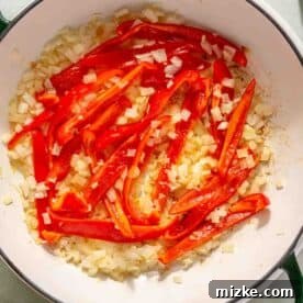 Spicy Thai Green Curry Chicken Rice Bowl 7 Chopped onions and red bell peppers cooking in a white skillet, surrounded by bowls of ingredients.