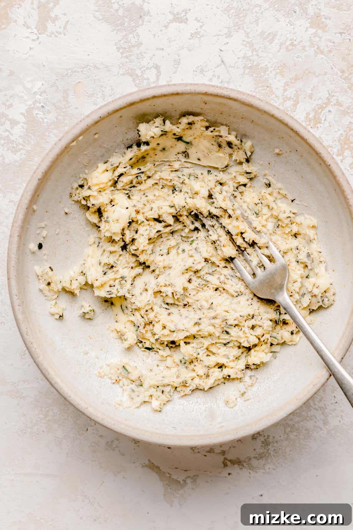 Caramelized Fig Chicken Skillet 4 A fork is mixing softened butter, minced garlic, and fresh rosemary in a small bowl to create the aromatic herb butter.