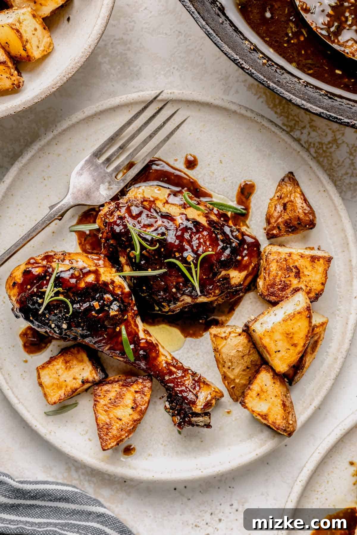 Caramelized Fig Chicken Skillet 9 Two pieces of fig glazed chicken served on a white plate with roasted potatoes and fresh rosemary, making for an inviting meal.