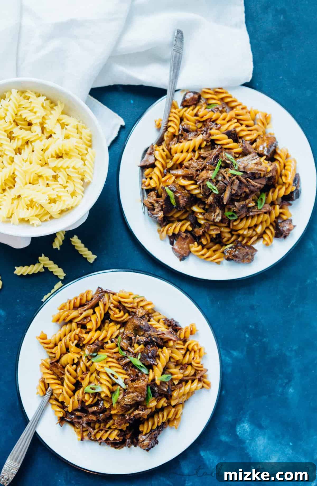 Tender Korean Beef Ragu 4 Hands stirring Pressure Cooker Korean Beef Ragu with rotini pasta directly in the Instant Pot liner, showing the thick, savory sauce clinging to the beef and noodles.