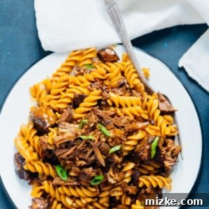 A top-down shot of Pressure Cooker Braised Korean Beef Ragu with rotini pasta in a bowl, showing the rich sauce, tender beef, and fresh scallion garnish.