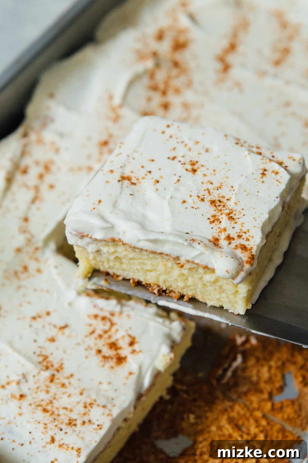 Holiday Eggnog Tres Leches 5 A slice of eggnog tres leches cake being gently lifted out of the baking pan with a metal serving spatula, showcasing its luscious layers.