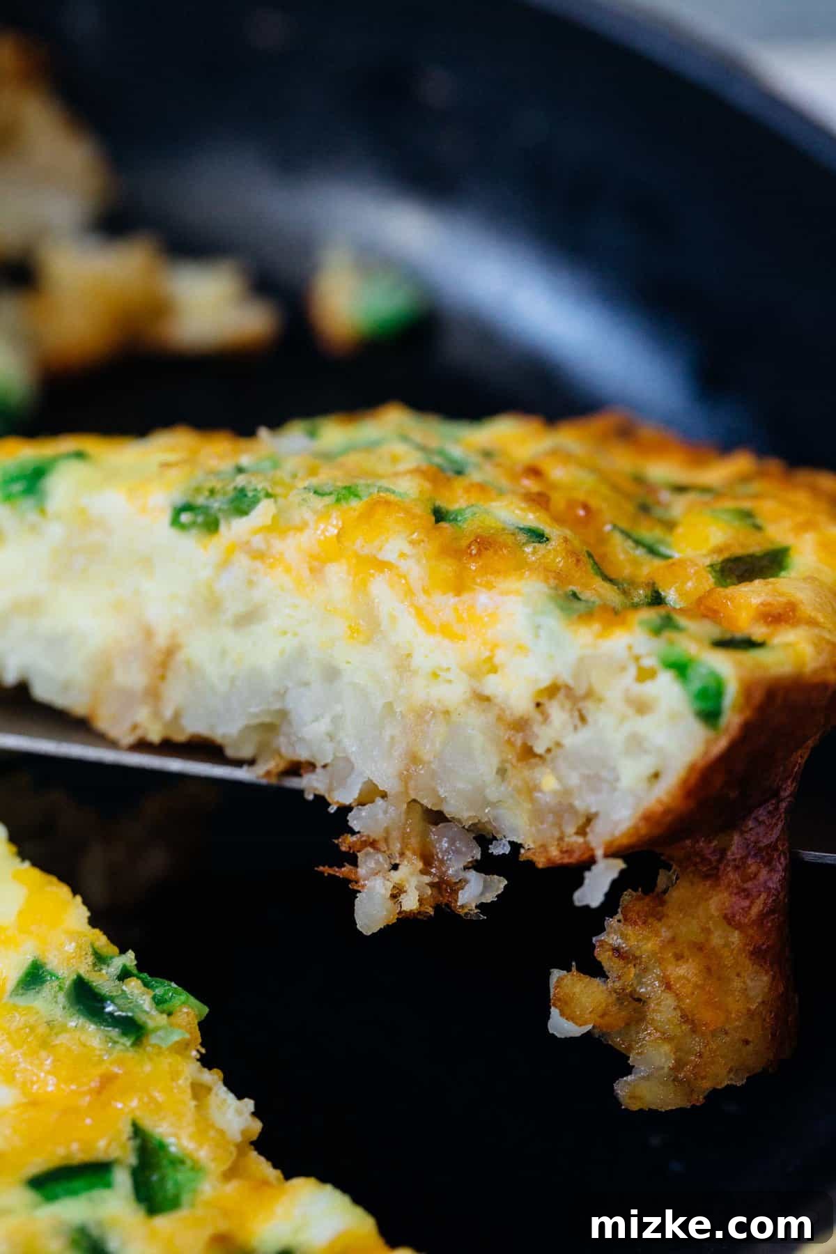 This one-pan cheddar jalapeno tater tot frittata recipe puts a fun twist on a potato and egg frittata, baked inside a crispy tater tot crust. A slice of frittata lifted from a cast iron skillet.