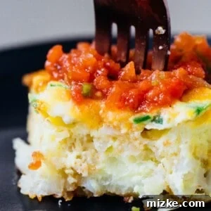 A fork stuck into a slice of cheddar jalapeño tater tot frittata on a black plate.