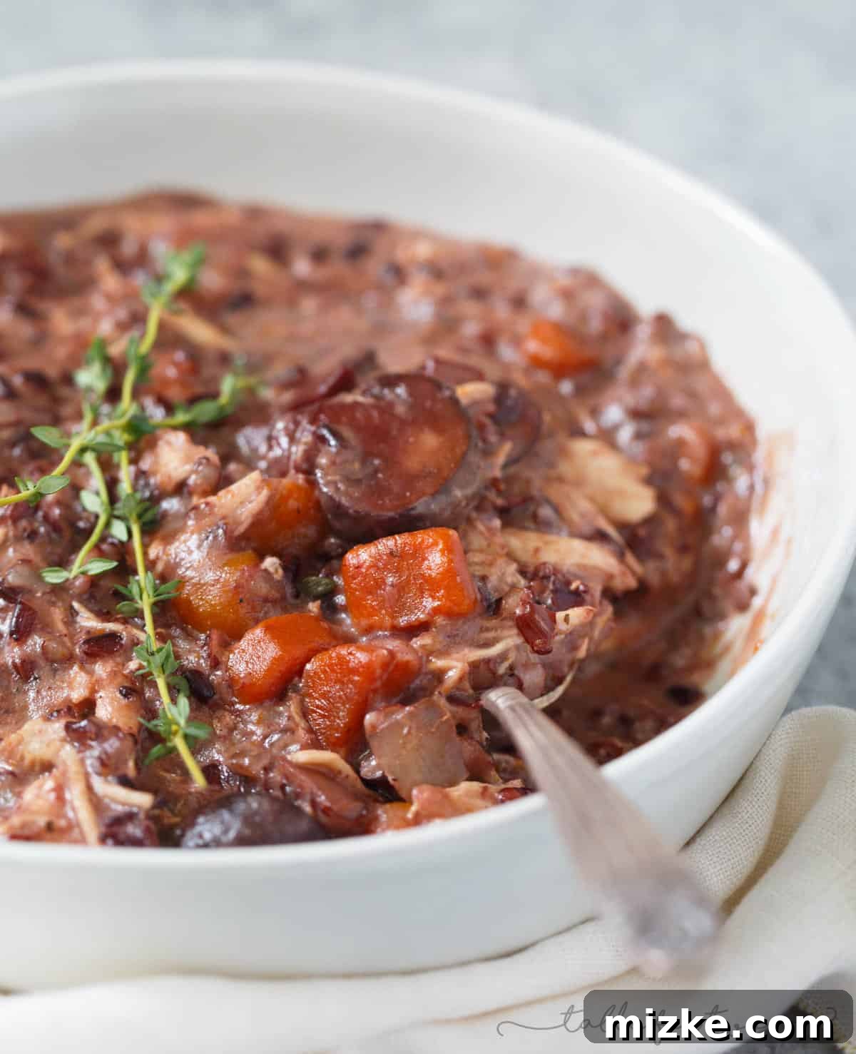 Velvety Instant Pot Chicken Mushroom Wild Rice Stew 6 A large serving spoon dipping into a bowl of creamy Instant Pot mushroom and chicken wild rice stew, garnished with fresh herbs.