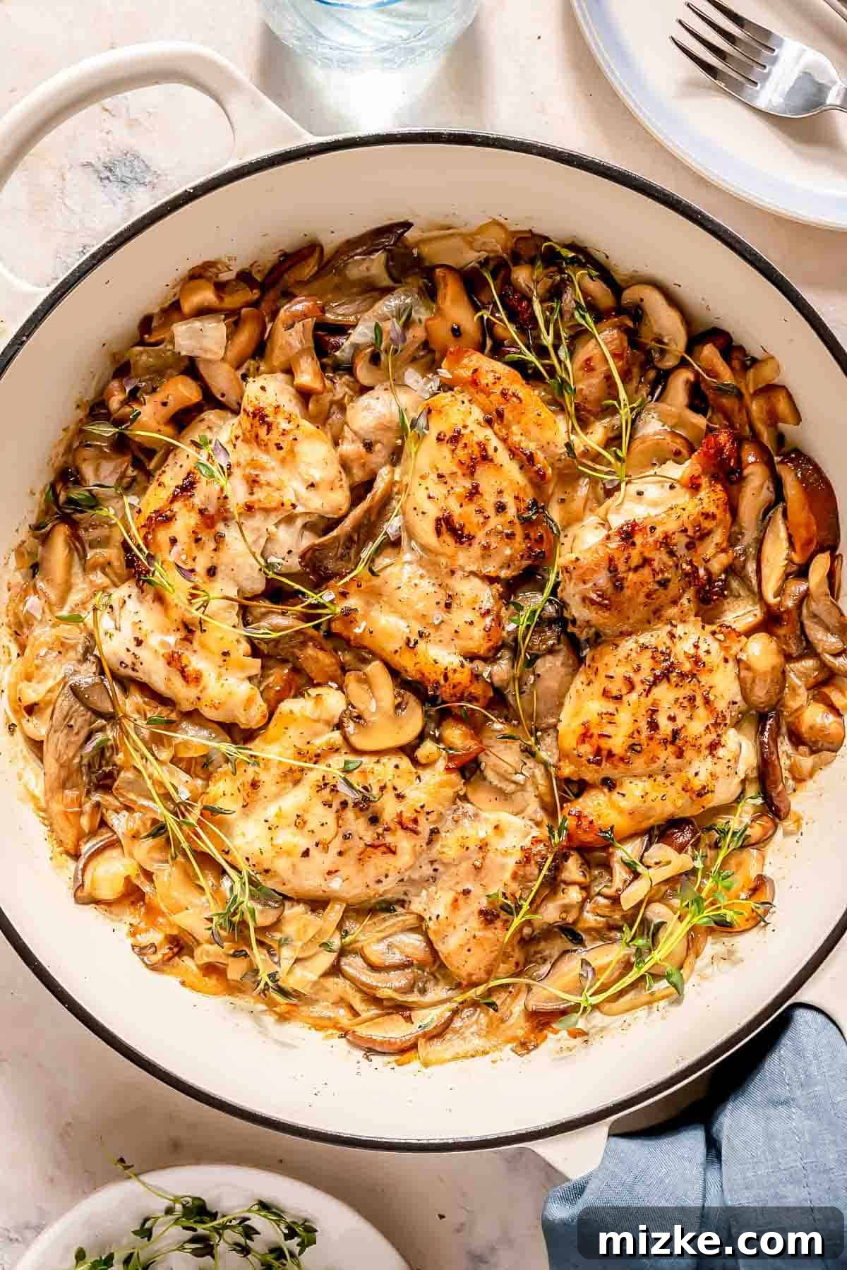Decadent Creamy Mushroom Chicken 2 A skillet filled with cooked chicken thighs, golden-brown mushrooms, tender onions, and fresh thyme sprigs, showcasing the rich, creamy sauce.