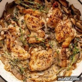 Decadent Creamy Mushroom Chicken 11 Chicken breasts cooked with mushrooms, onions, herbs, and cream sauce in a skillet, garnished with sprigs of thyme.