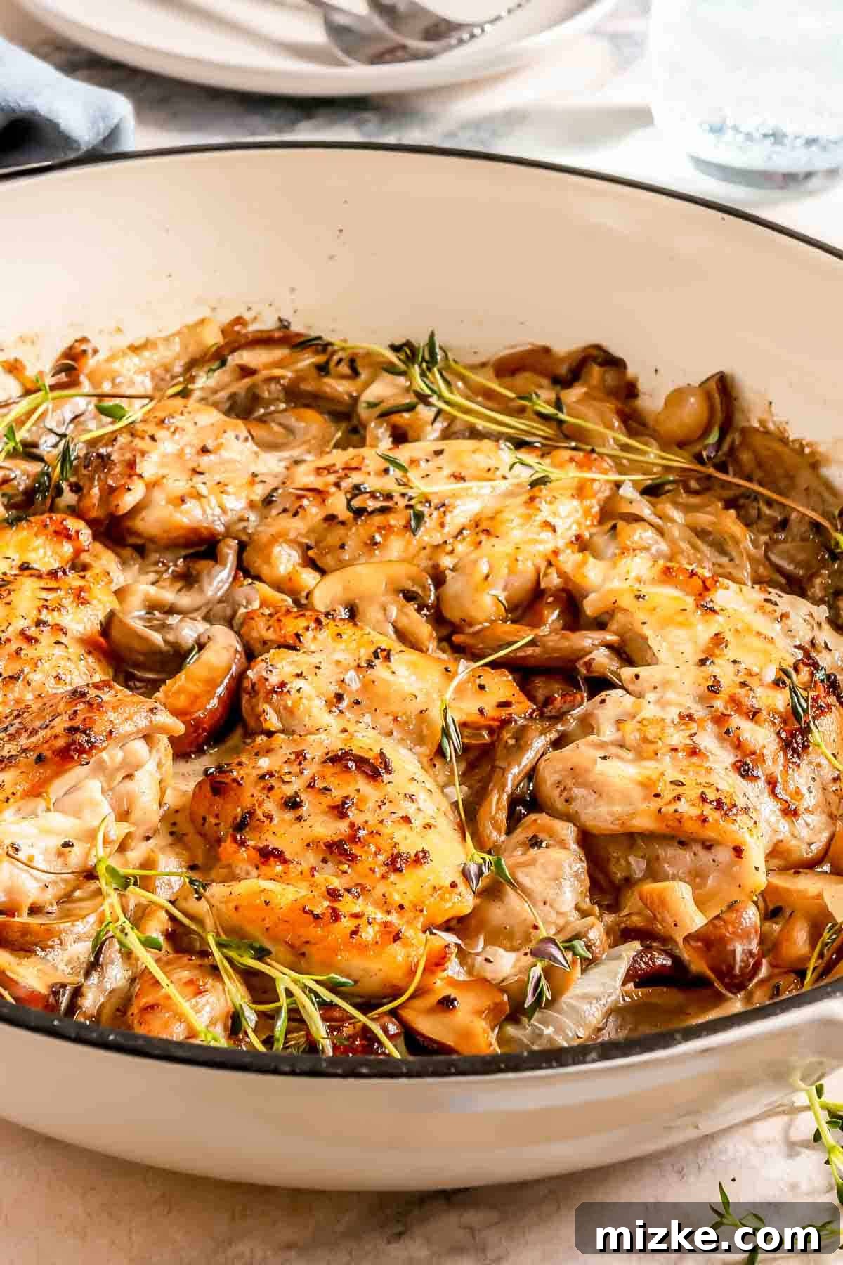 Decadent Creamy Mushroom Chicken 3 Beautifully cooked chicken thighs with sautéed mushrooms and onions in a gleaming skillet, garnished with fresh thyme, ready to be served.