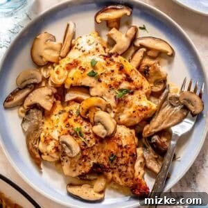 Creamy mushroom chicken served with a creamy mushroom sauce and garnished with fresh herbs on a round plate, accompanied by a fork and knife.