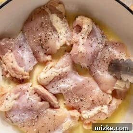 Velvety Mushroom Chicken 4 Raw, seasoned chicken thighs in a white pot with melted butter, shown with metal tongs, ready for cooking.