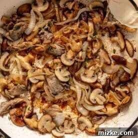 Velvety Mushroom Chicken 7 Sliced mushrooms and onions cooking in a white skillet, with white wine being poured in from a glass measuring cup.