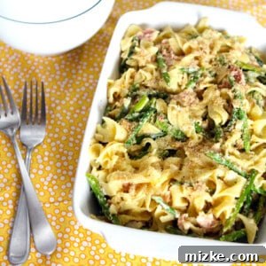 A close-up view of the finished Pasta Carbonara, showcasing the creamy sauce clinging to the egg noodles, interspersed with asparagus pieces and crispy pancetta, topped with golden breadcrumbs.