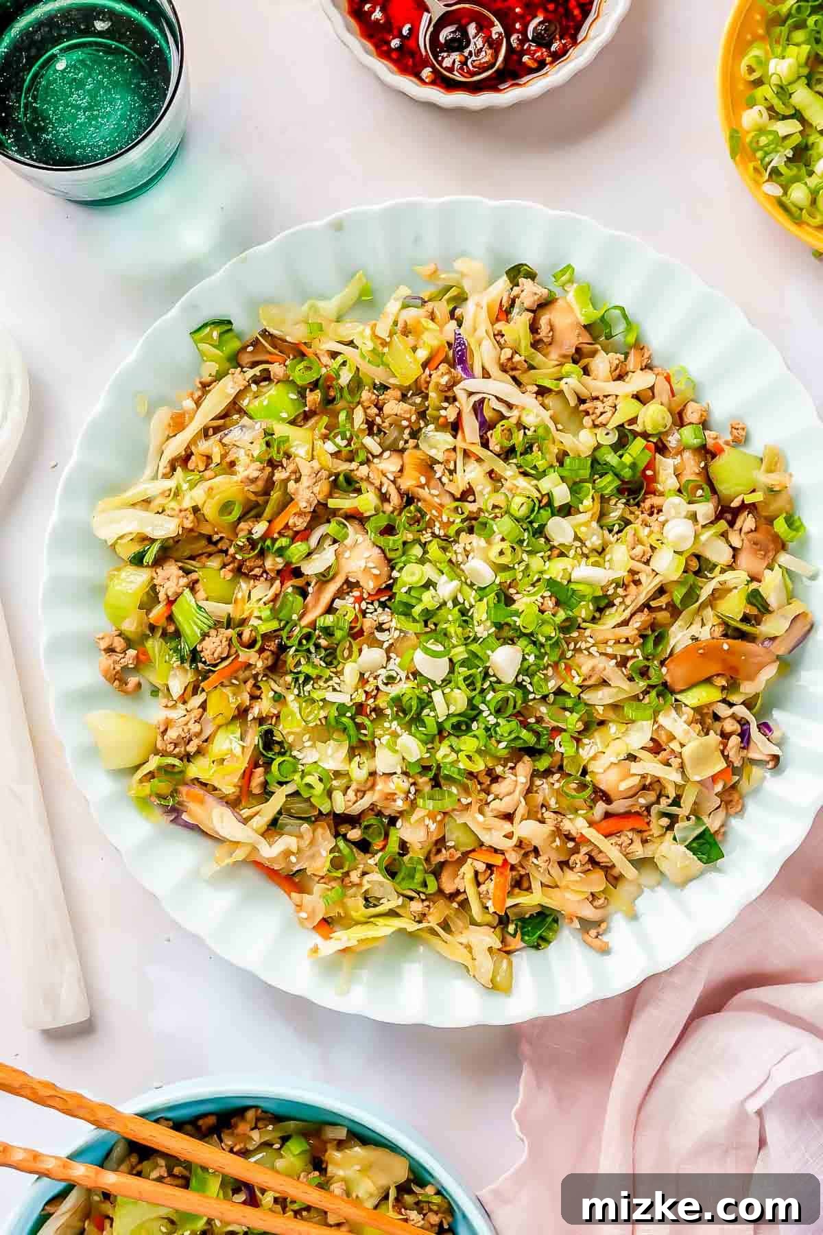 Delicious egg roll in a bowl filling on a scalloped blue plate, garnished with fresh scallions and white sesame seeds, ready to be served.
