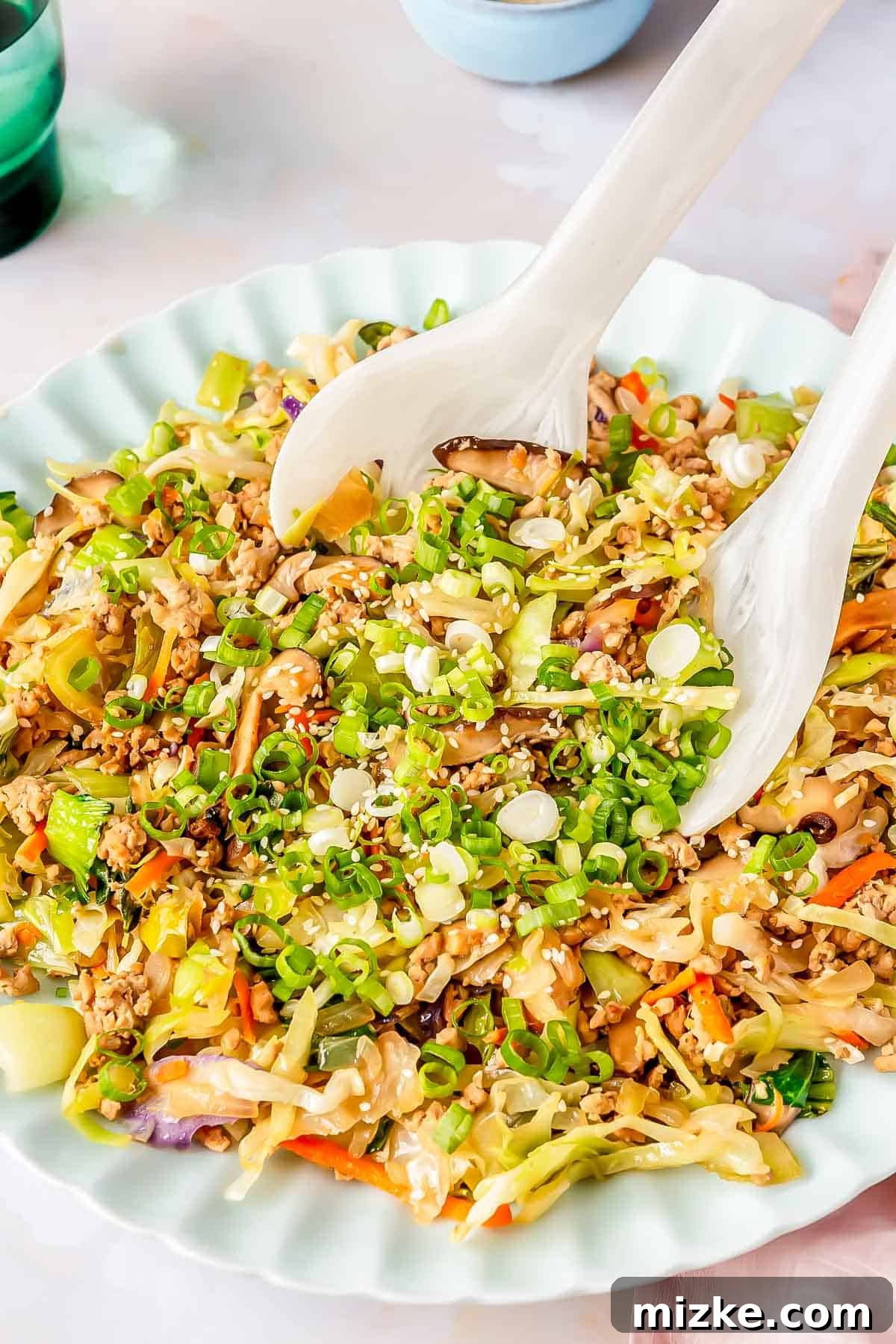 Two white melamine spoons scooping out the hearty egg roll in a bowl filling from a scalloped plate, showcasing the rich texture.