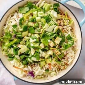 Baby bok choy and coleslaw mix being added to the skillet with the pork and aromatics, ready to be cooked down.
