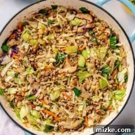 Cooked down cabbage and bok choy mixture in an enameled cast iron skillet, with soy sauce coating the ingredients.