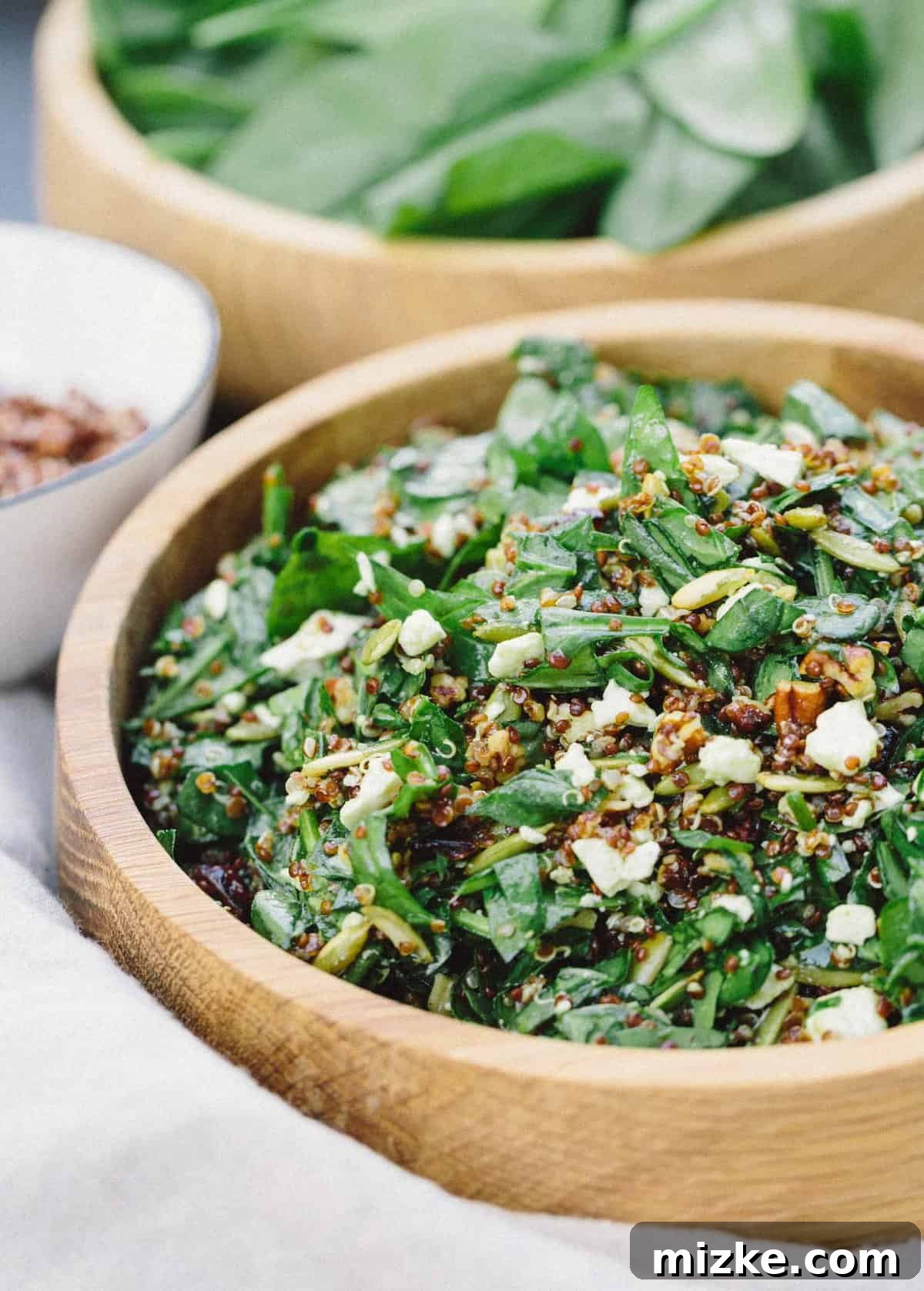 Nutty Spinach and Quinoa Salad: Freshly prepared and ready to serve, a perfect blend of healthy ingredients and satisfying flavors. #saladbowls #vegetarianfood #healthymeals #quickandeasy A bowl of nutty spinach and quinoa salad on a wooden table, featuring fresh ingredients and a rustic presentation.