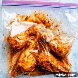 Raw chicken drumsticks marinating in a sealed plastic bag on a textured blue surface.