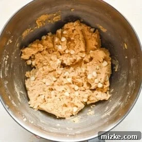Heavenly White Chocolate Chip Cookies 9 White chocolate chips combined in a metal stand mixer bowl with cookie dough.