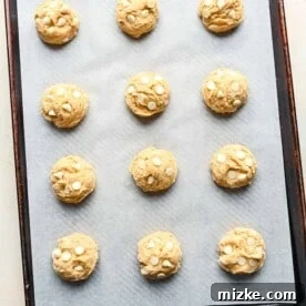 Heavenly White Chocolate Chip Cookies 10 Scooped white chocolate chip cookie dough on a metal baking sheet lined with parchment paper.