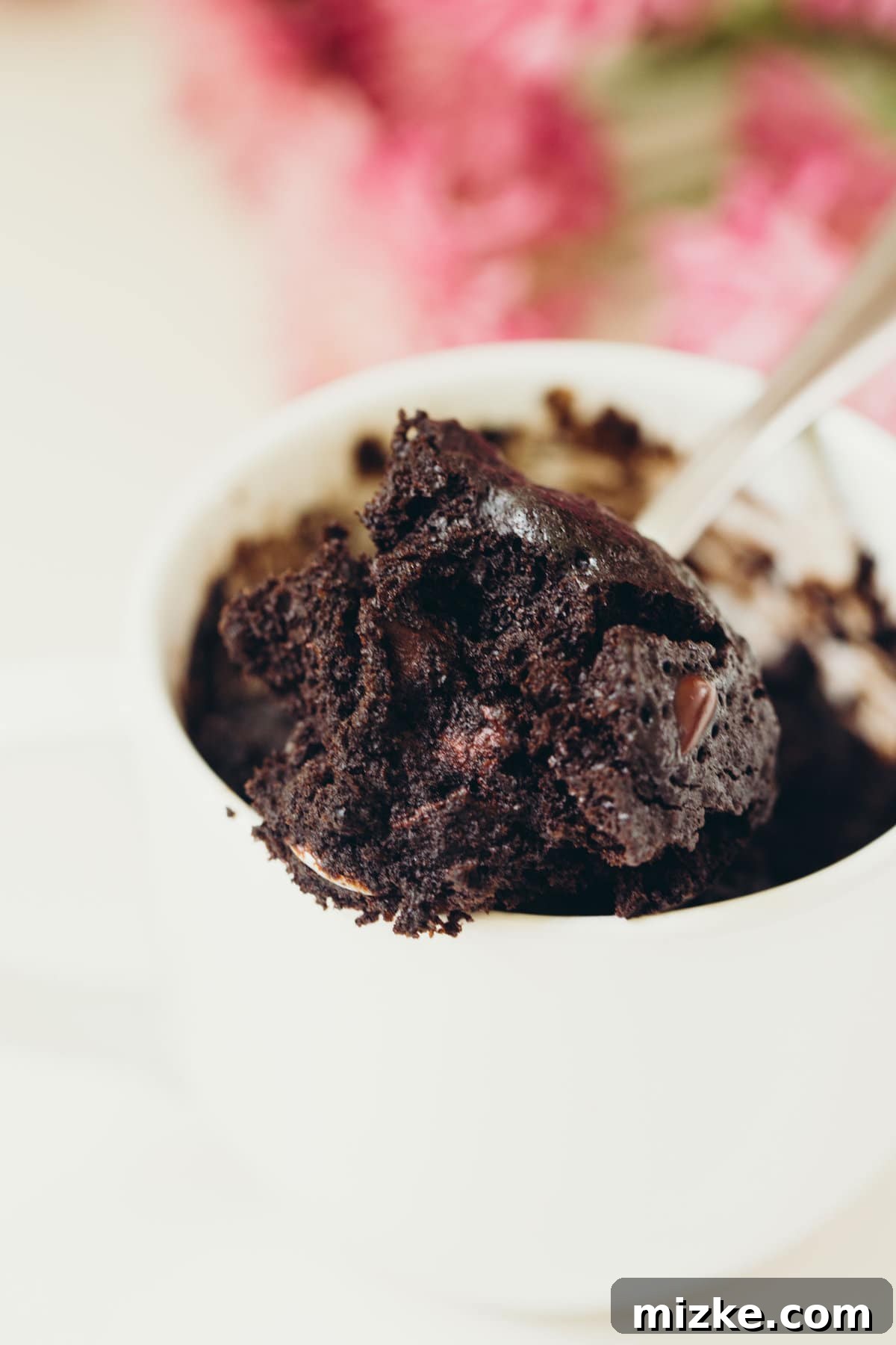 Experience the deep, rich flavor of our Dark Chocolate Mug Cake. Close-up of a dark chocolate mug cake with a spoon, showing its moist interior and tempting texture. Keywords: dark chocolate, cake in a mug, mug cake, chocolate mug cake, dessert for one, single serving, quick dessert.