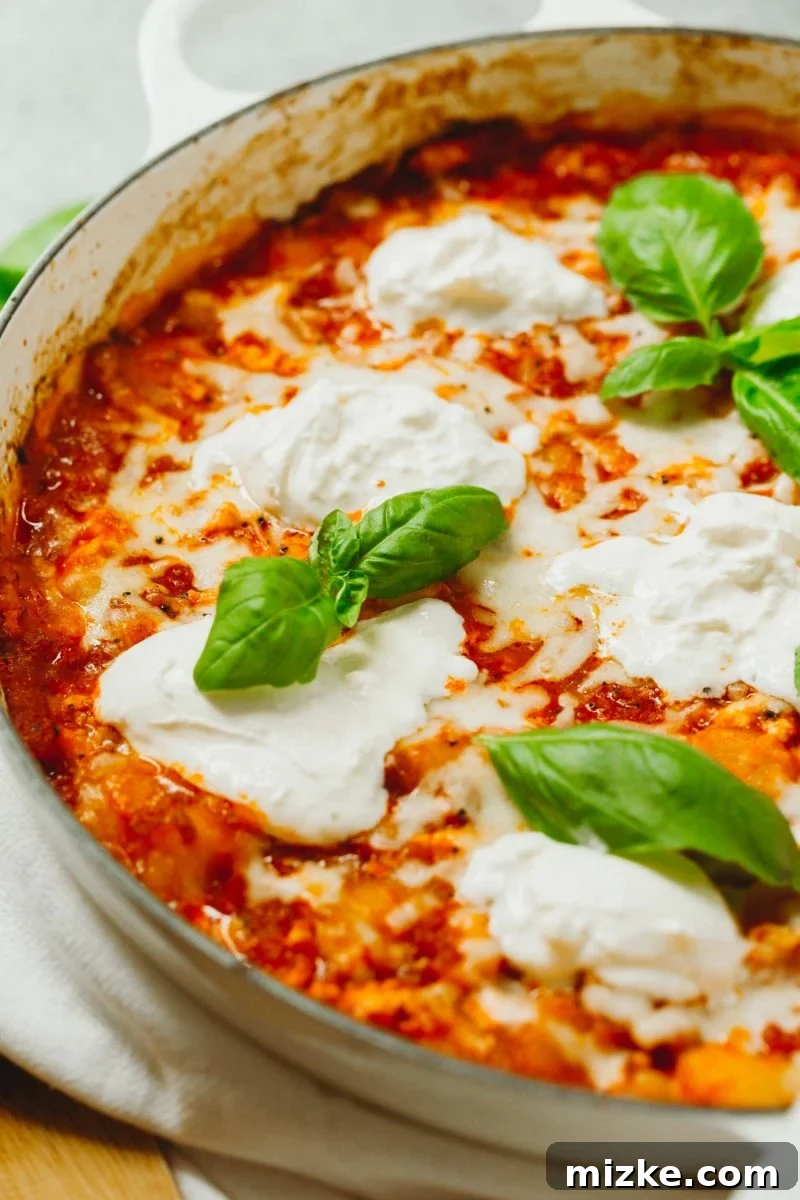 An easy dinner idea is this low-carb chicken parmesan gnocchi bake that is put together in one skillet! A great way to use that cauliflower gnocchi if you need ideas on how to use it! A vibrant close-up of the delicious low-carb chicken parmesan gnocchi bake, showcasing melted cheese and fresh basil atop cauliflower gnocchi.